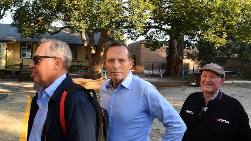 Three men stand in a queue at a school.