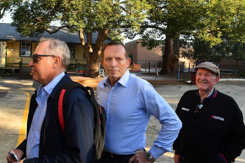 Three men stand in a queue at a school.