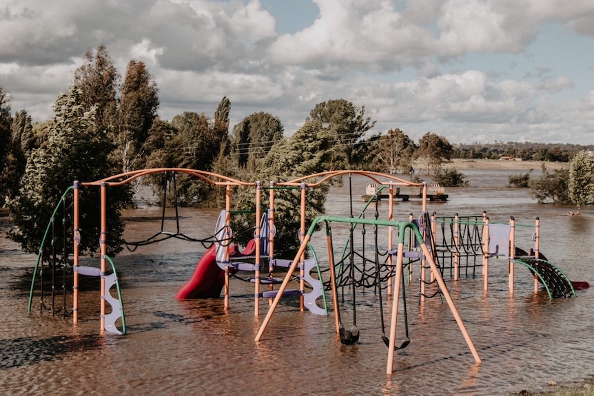 a flooded playground is shown in a park with trees and area behind the playground also flooded