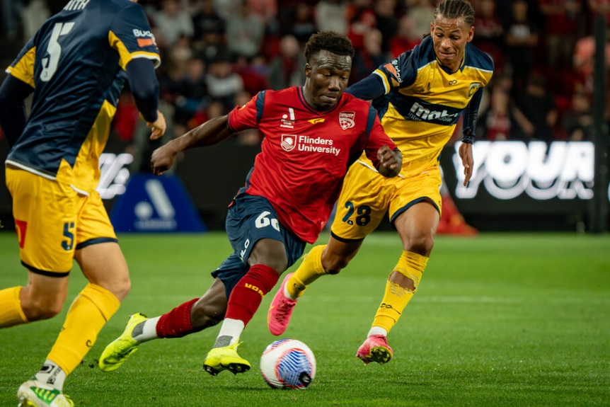 Adelaide United player Nestory Irankunda dribbles past Central Coast players in an A-League match.