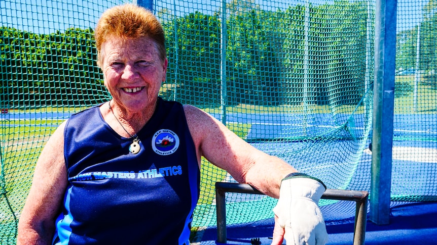 An older woman smiles for the camera wearing a NSW Masters Athletics shirt