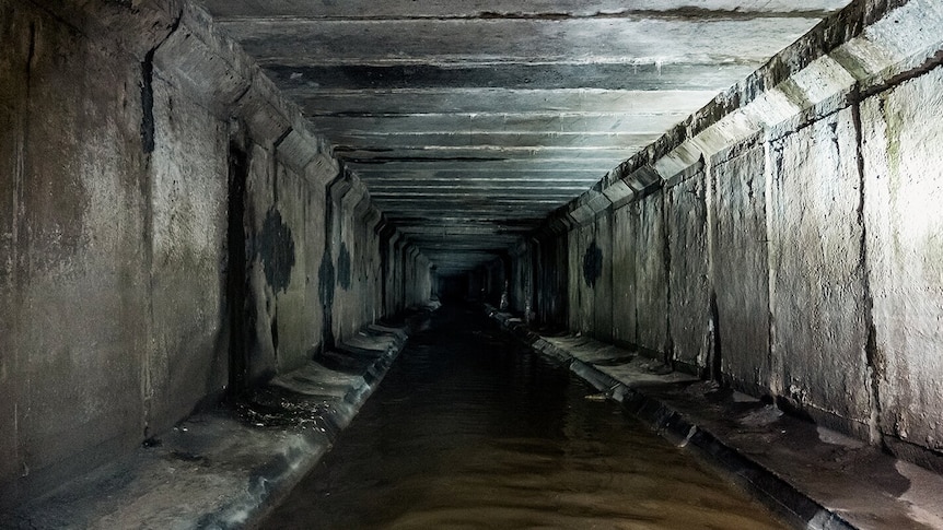 A dark, large and empty sewer system underground, with some sewerage running through it