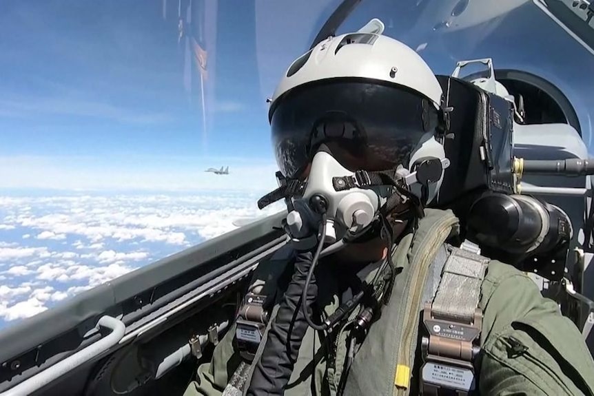 A Chinese air force pilot flies a military jet in full uniform and helmet.