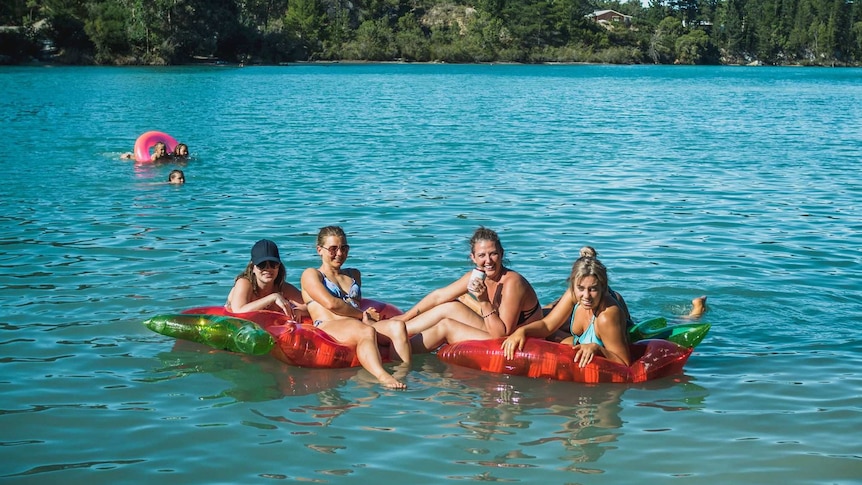 Four women sit on inflatable rafts and toys in a blue lake