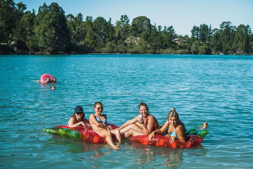 Four women sit on inflatable rafts and toys in a blue lake