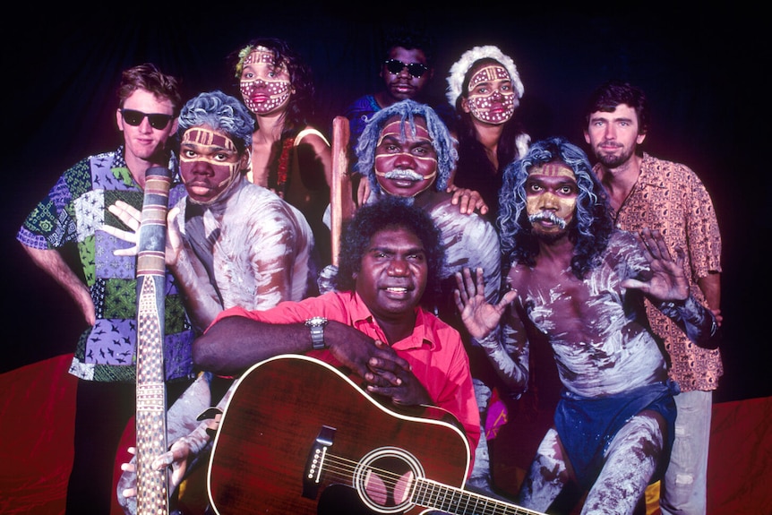 a group of aboriginal and non-indigenous artists posing with guitars and didgeridoos