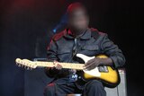 Dr G Yunupingu performs sitting on stage with a guitar.