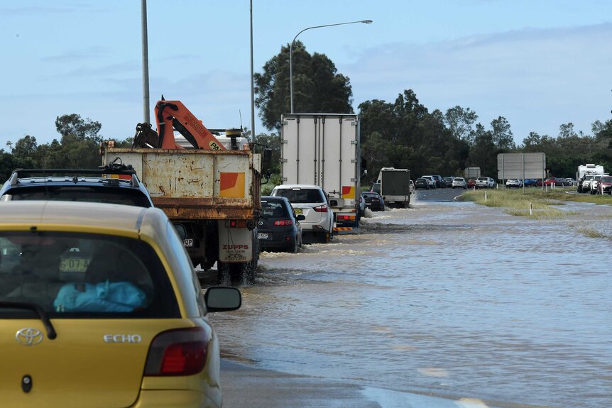A line of traffic drives through floodwaters on the pacific highway near tweed heads