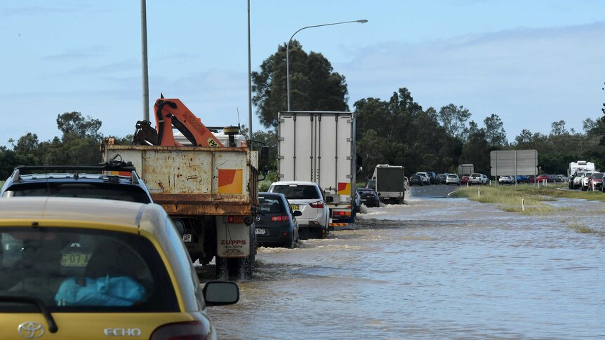 A line of traffic drives through floodwaters on the pacific highway near tweed heads