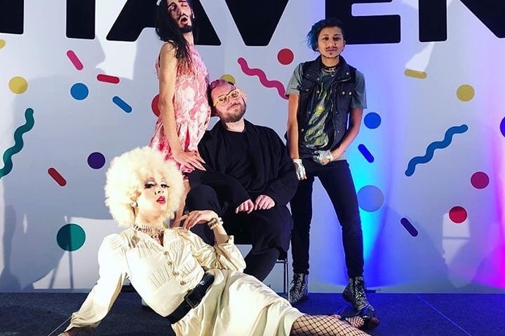 Performers in fabulous costume pose in front of a colourful sign that reads HAVEN.