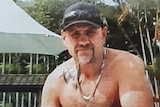 Dwayne Johnstone without shirt, wearing black hat, sunglasses on hat and chains around neck.