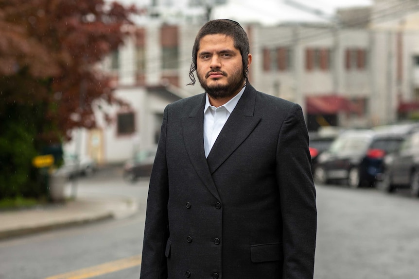 A man in a suit and skull cap stands on a suburban US street