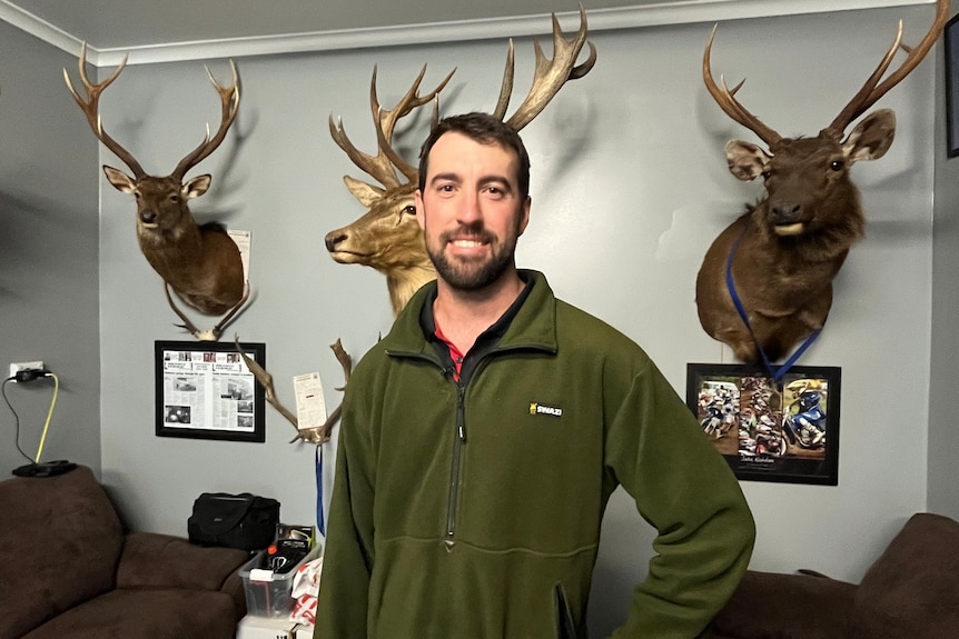 A man standing in front of deer trophies mounted on a wall.