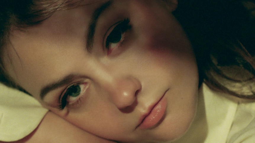 Very close up photo of Angel Olsen's face as she lies on her hand