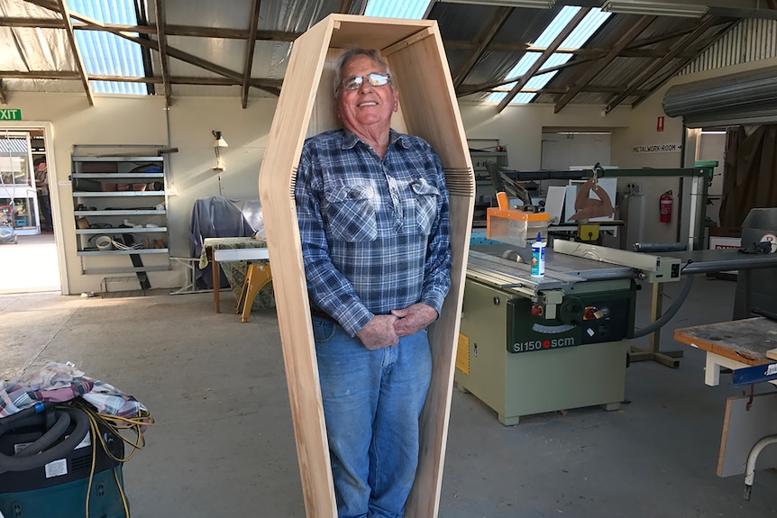 A man standing in a wooden coffin showing a do-it-yourself-coffin to reduce funeral costs