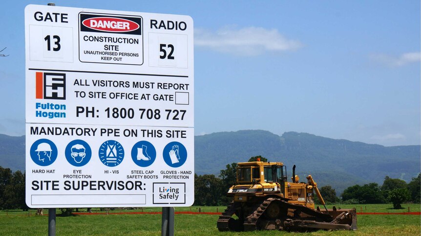 A construction site sign and bobcat in green farmland.