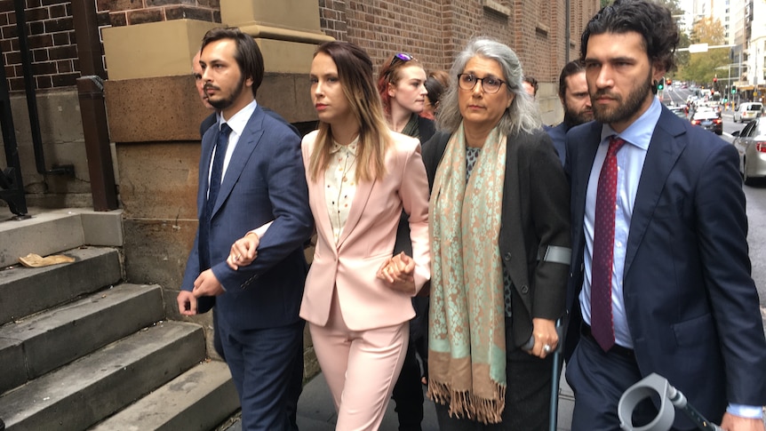 a woman in a pink suit holding hands with people as she is walking into court