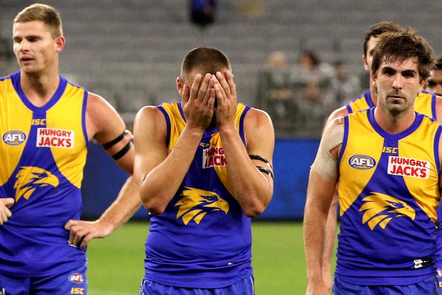 Dom Sheed and a handful of West Coast Eagles teammates walk off the field with Sheed holding his head in his hands.