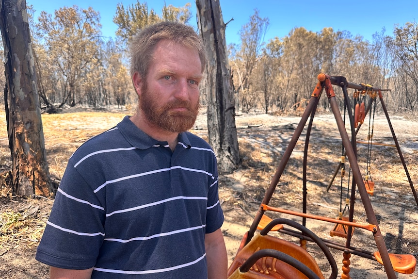 Ben stands near a fire-damaged child's swing set on his property.