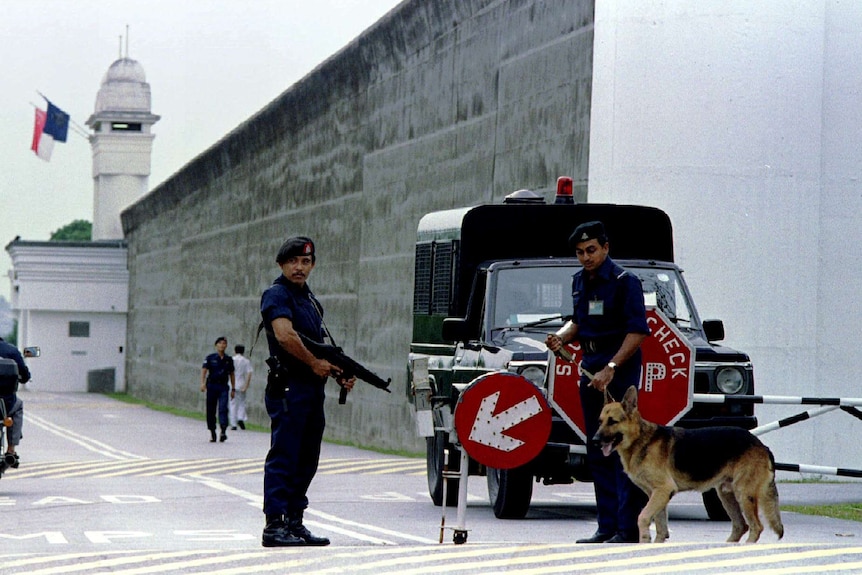Two guards and a dog standing at a prison gate