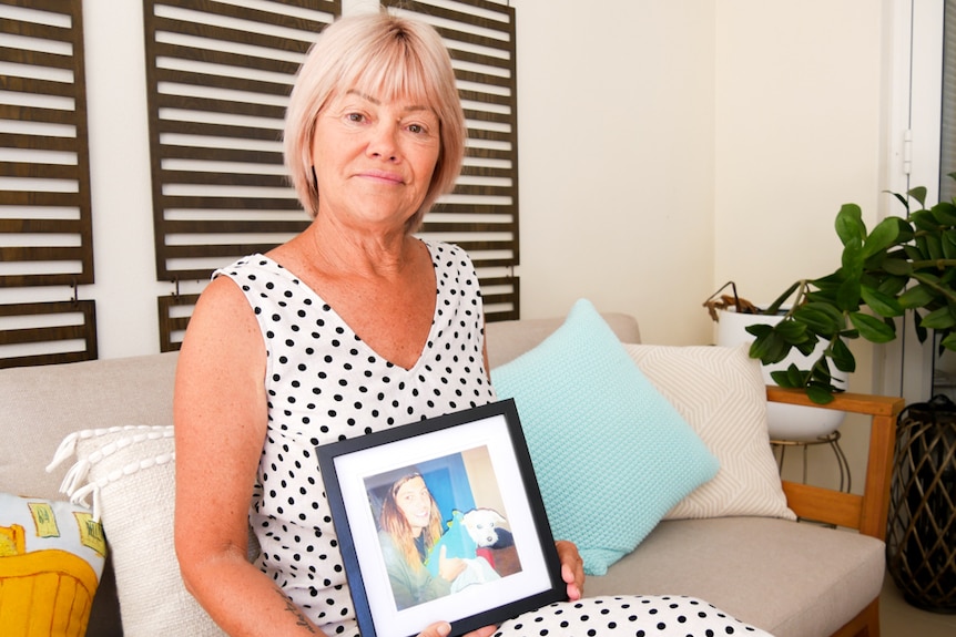 A woman sitting on a couch holding a picture of her son.