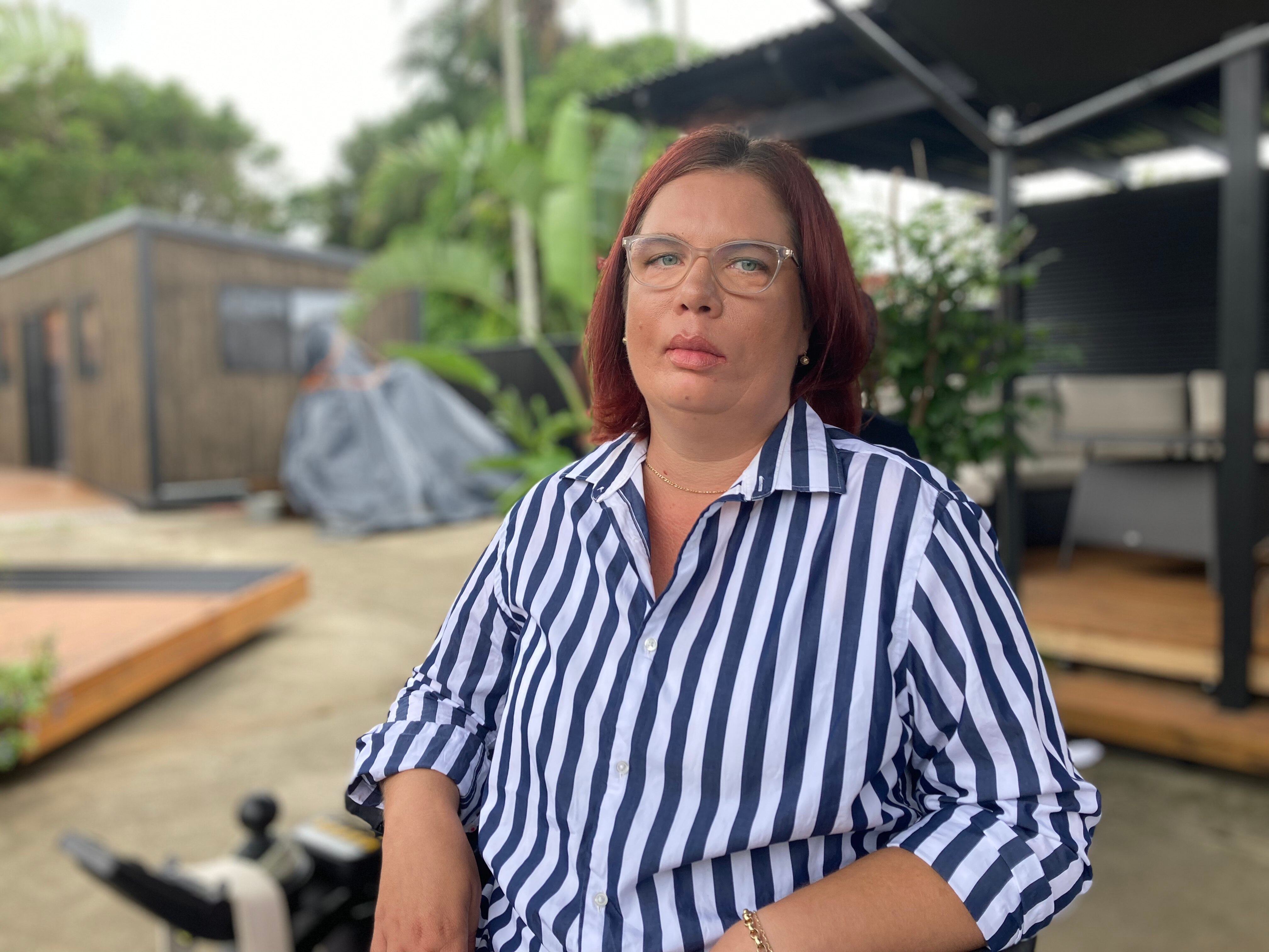 A woman wearing glasses and a blue and white-striped shirt, seated and unsmiling.