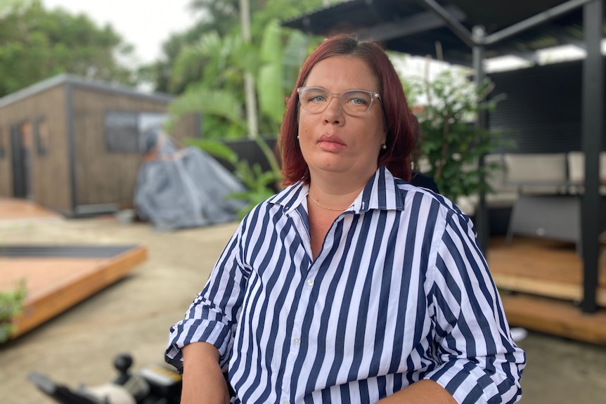 A woman wearing glasses and a blue and white-striped shirt, seated and unsmiling.