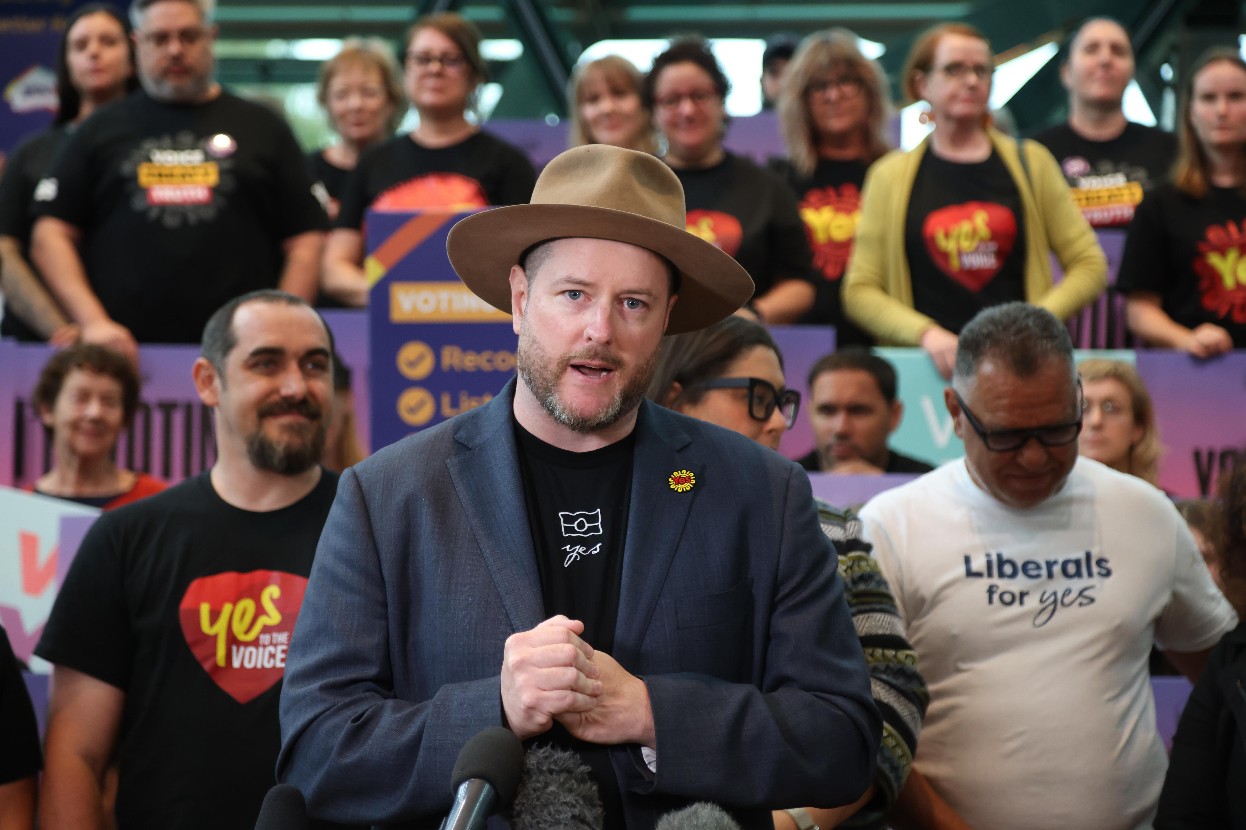 Yes campaigner Marcus Stewart speaking at an event in front of people holding signs in support of the Voice to Parliament