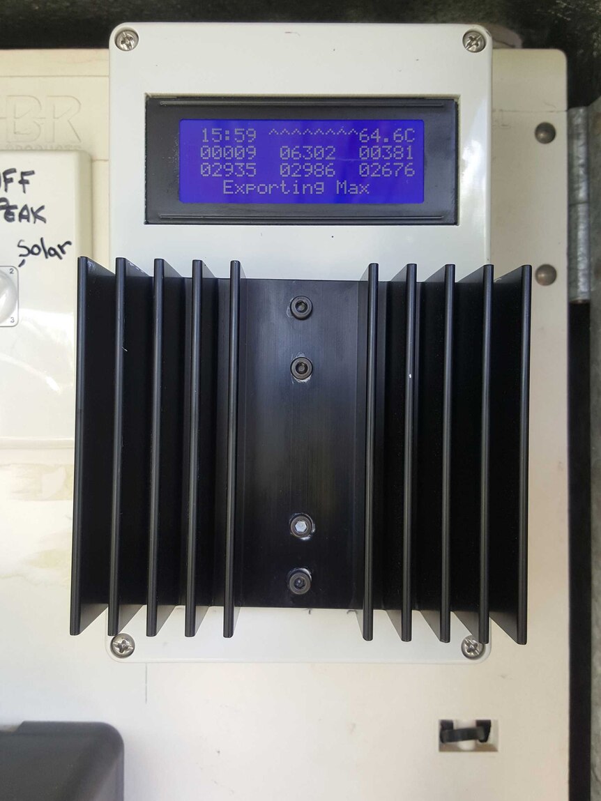 A close-up of a  solar energy diverting device, a small black and white box with a blue LCD panel on it.
