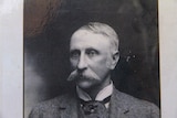 An old black and white photo of a moustached man in a suit.