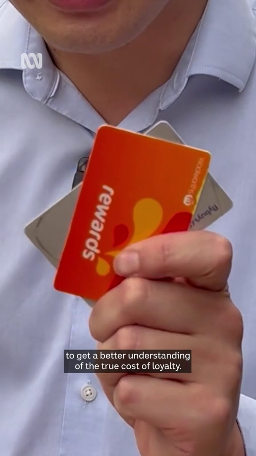 A man's hand holds up supermarket loyalty cards to the camera, his shaven chin and blue shirt are visible in the background