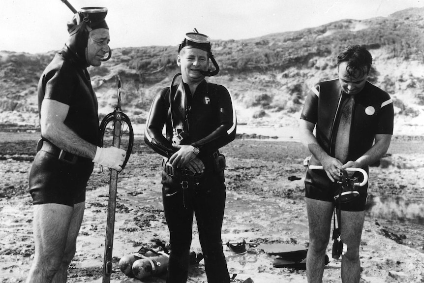 Black and white photo of Holt, McAlpine and Tingle in wetsuits and snorkelling gear at Portsea beach.