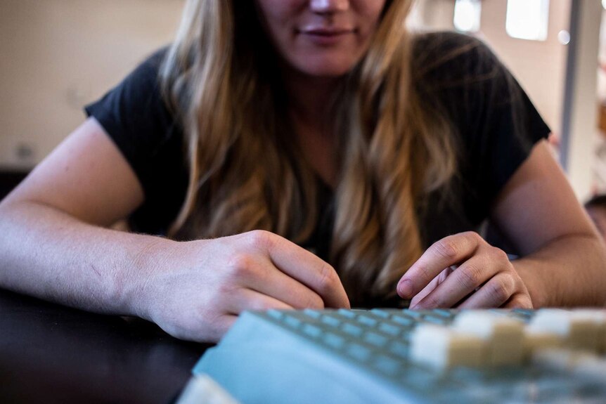 A woman with blonde hair is out of focus but her hands, holding game tiles, are in focus while she thinks.