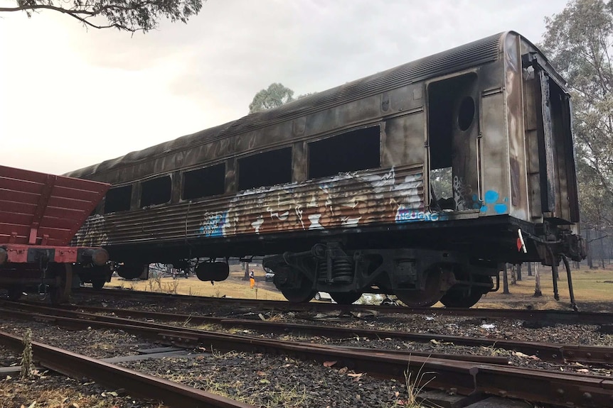 A scorched train carriage sits on the rails with burnt ground around it.
