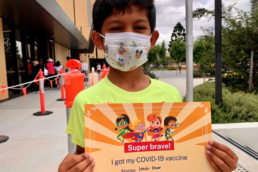 A boy wearing a mask holds a vaccine certificate