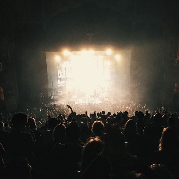 Photo of a performing arts space, the space is crowded and dark and the stage is brightly lit