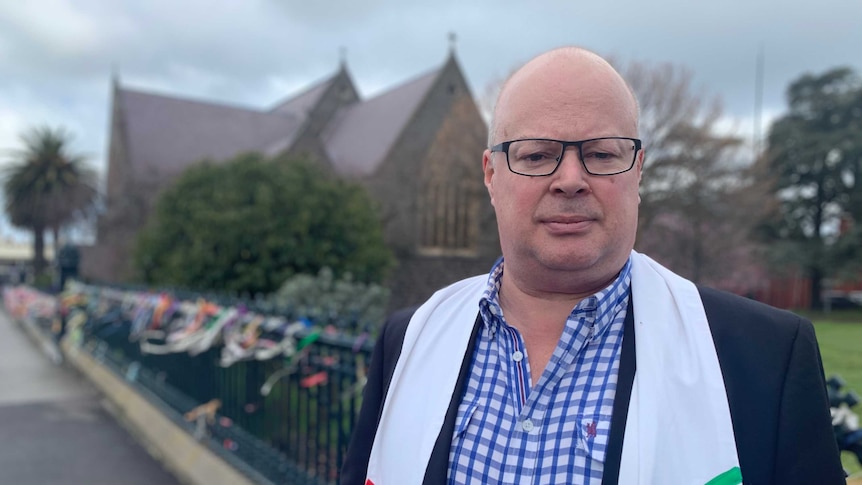 Father Andrew Hayes standing in front of his church in Ararat, with ribbons attached to the fence