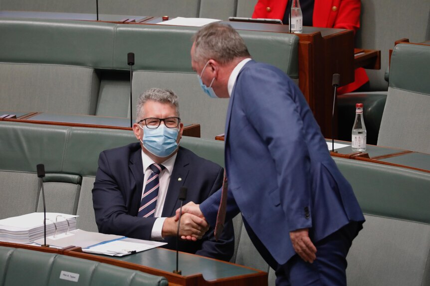 Keith Pitt, who is sitting down in the house of representatives wearing a mask, shakes Barnaby Joyce's hand