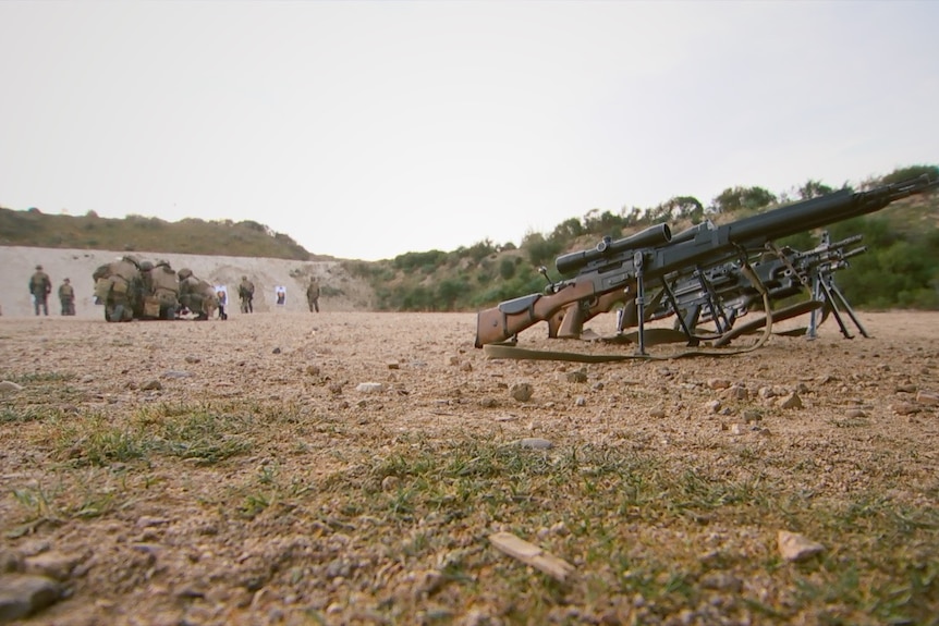 Legionnaires crouch down in a huddle on a firing range.