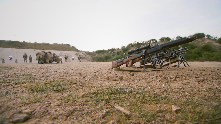 Legionnaires crouch down in a huddle on a firing range.