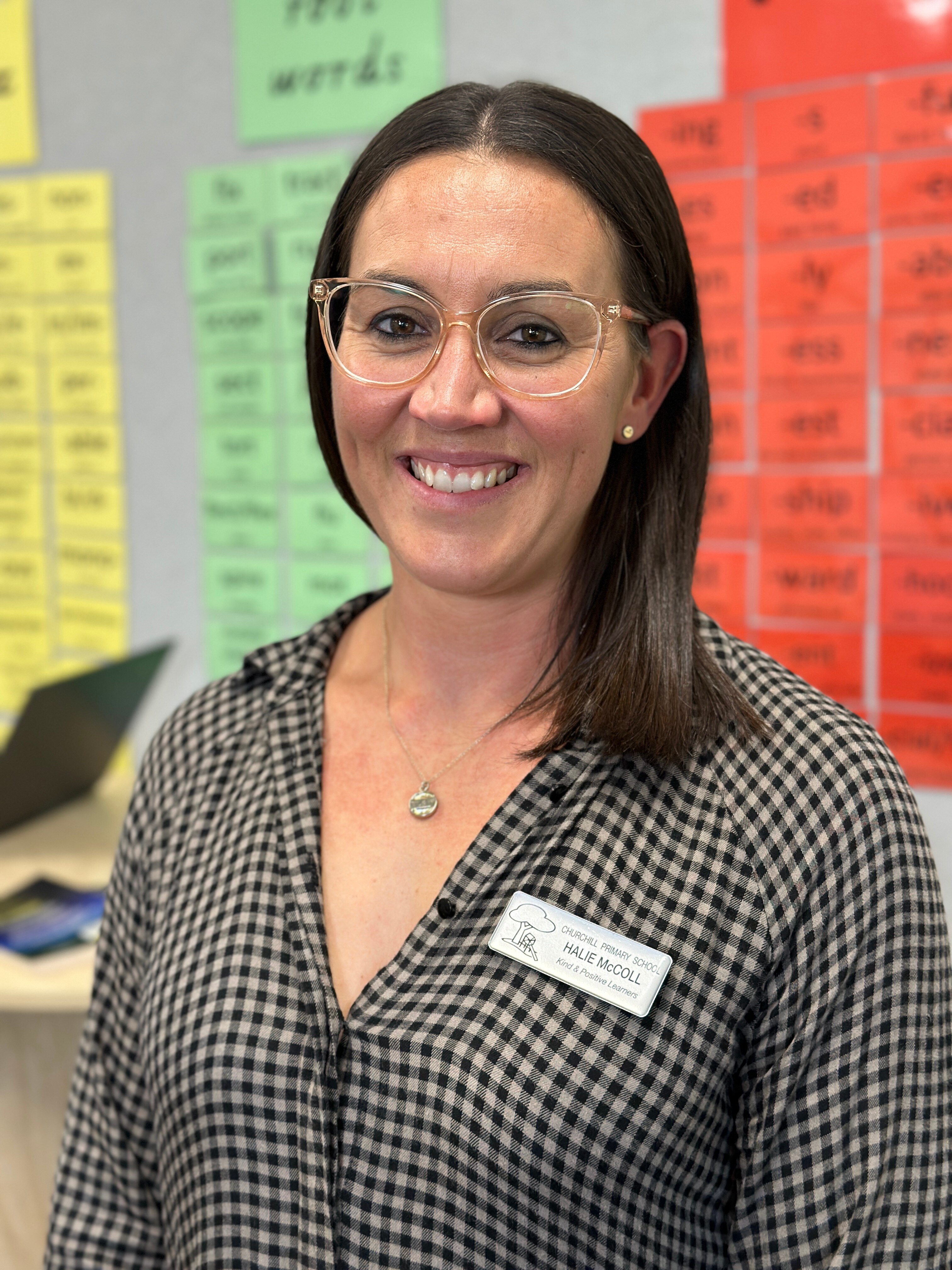 A young white woman with long brown hair and glasses standing in a classroom