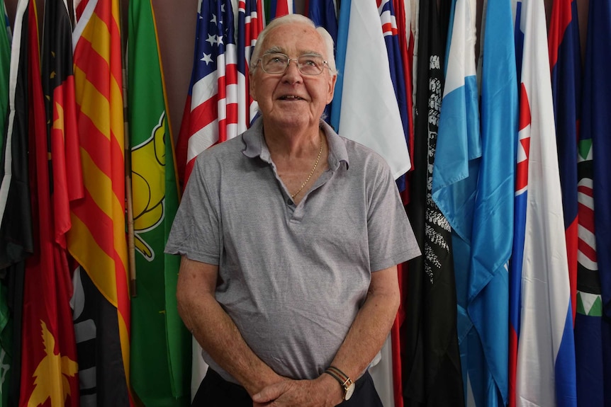82-year-old Ron Strachan standing in front of wall of colourful flags.