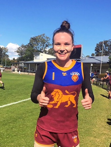 Emily Bates smiling and giving both thumbs up as she wears long sleeves and a Brisbane Lions jersey.