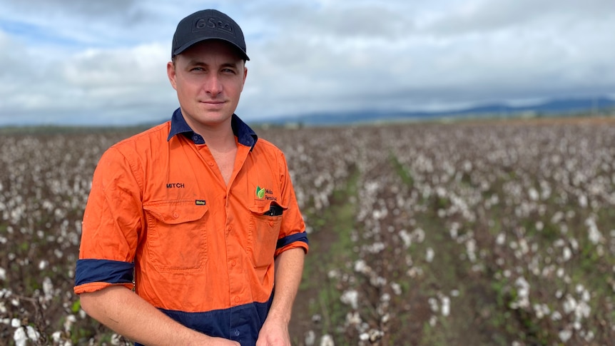 Man stands in orange workshirt in front of flood affected cotton crop