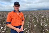 Man stands in orange workshirt in front of flood affected cotton crop