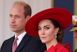 Prince William and Princess Catherine attend a ceremony. Catherine is wearing a large red hat.