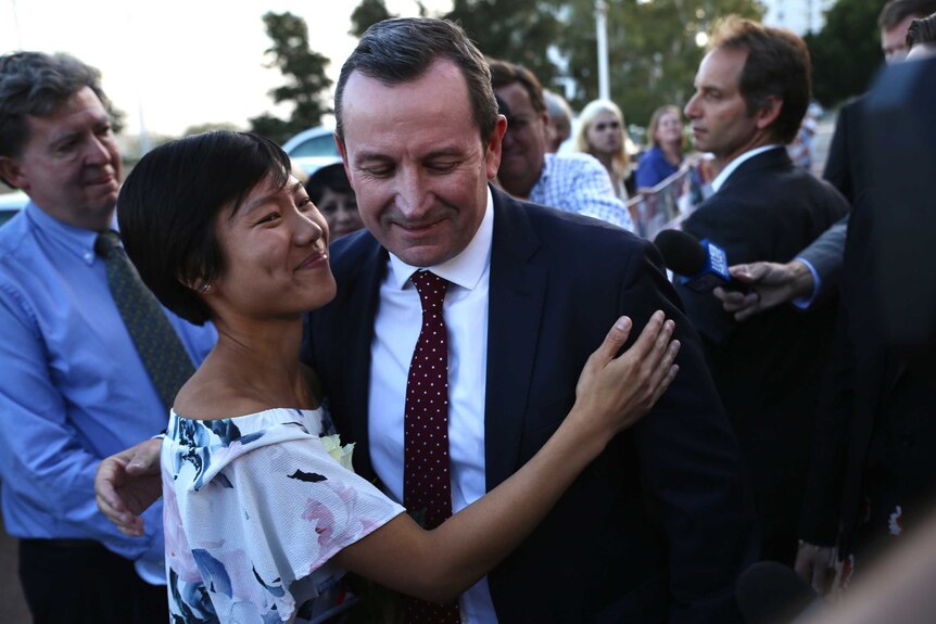 A woman smiles and hugs a man in a suit in the middle of a crowd