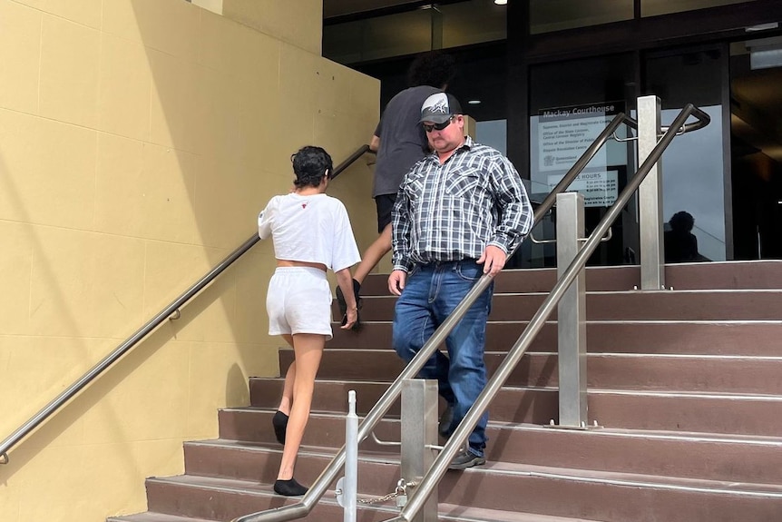 A man in a check shirt and jeans walking down the stairs at the Mackay Courthouse.