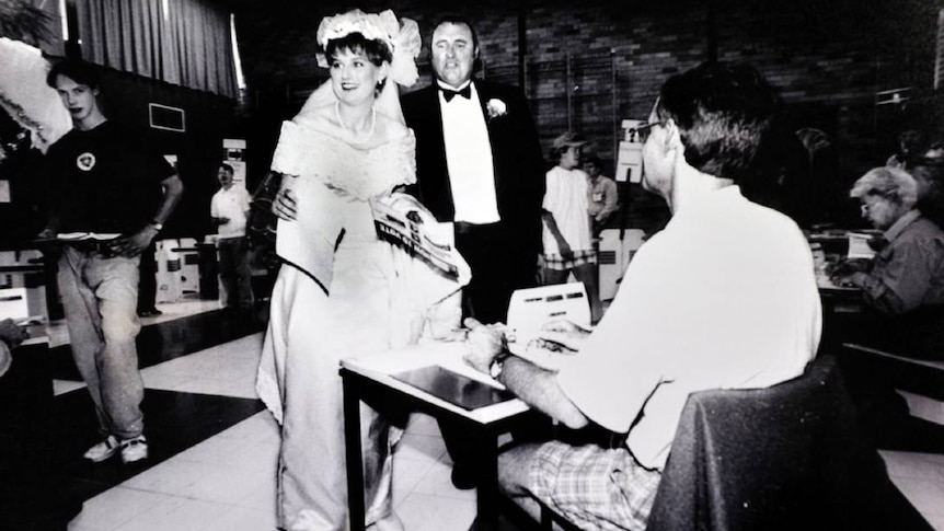 A black and white image of a young woman in a wedding dress at a polling station.