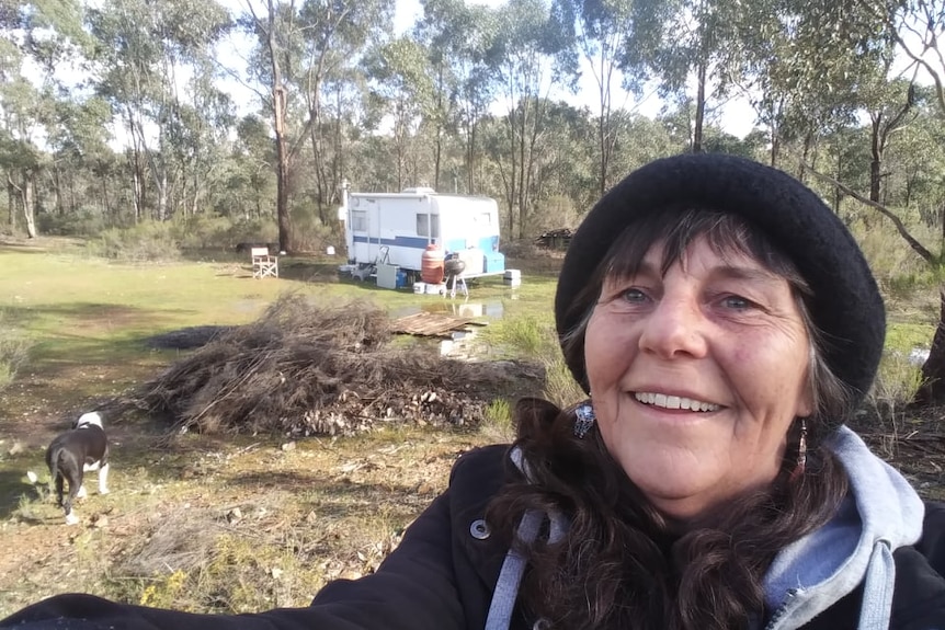 A woman poses in an outdoor area, with a caravan visible in the background.